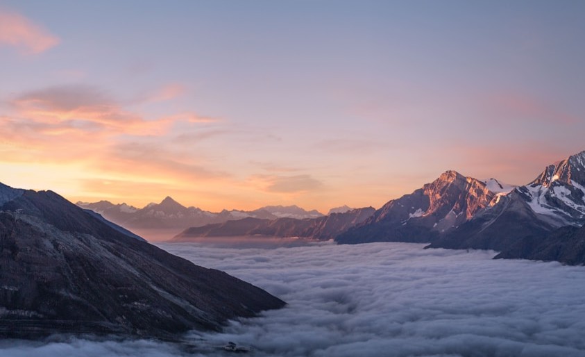 Snow-capped mountain peaks rising above a layer of clouds at sunrise with pink and orange sky